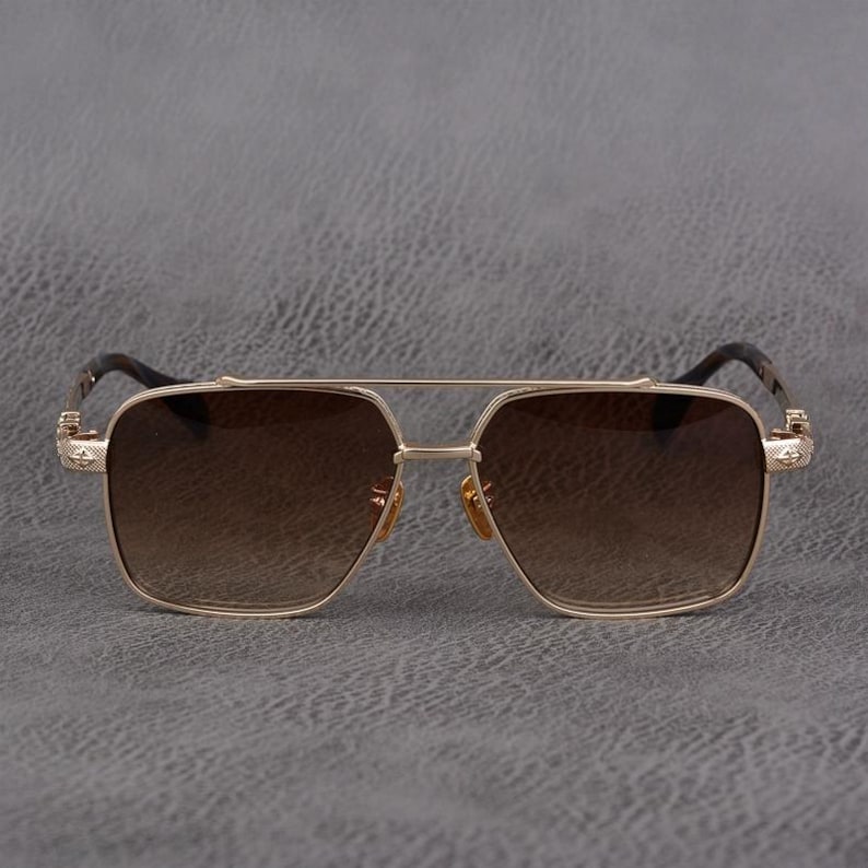 Puede incluir: Gafas de sol doradas con lentes degradadas marrones. Las gafas tienen un doble puente y lentes cuadradas. Las patillas son de color marr&oacute;n oscuro y presentan detalles decorativos. El dise&ntilde;o es moderno y elegante.