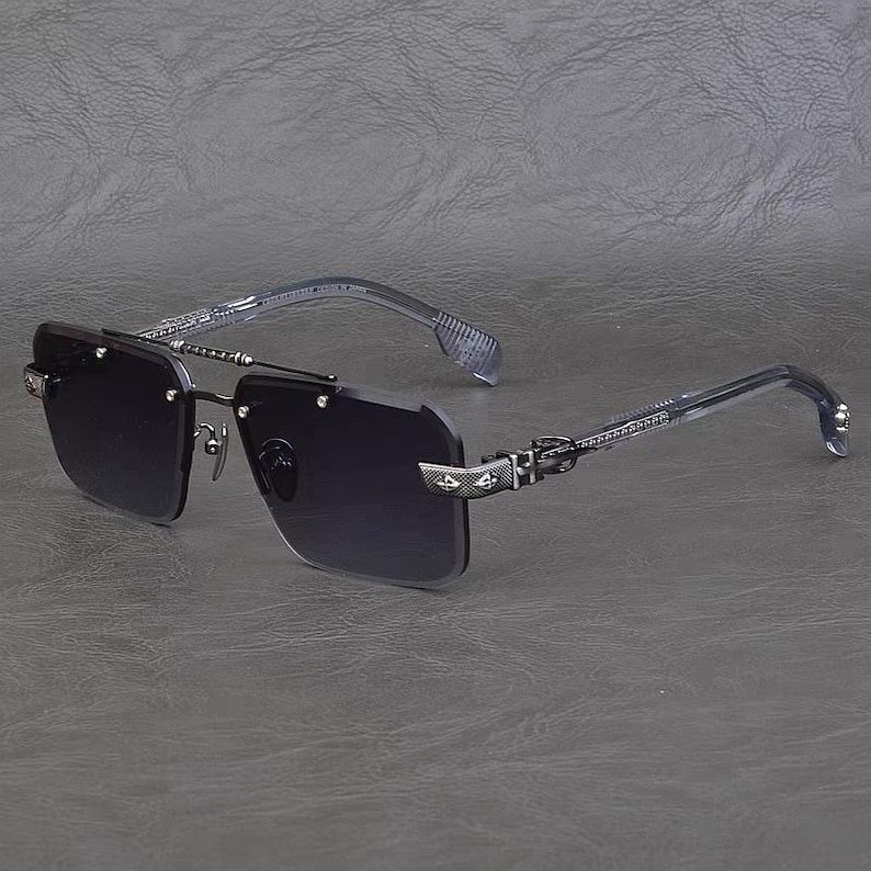 Puede incluir: Gafas de sol sin montura con lentes oscuras y detalles met&aacute;licos plateados. Las patillas y el puente presentan detalles intrincados. Las gafas de sol tienen forma rectangular y un dise&ntilde;o moderno.