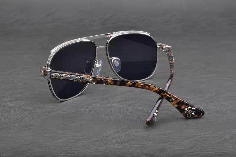 Puede incluir: Gafas de sol estilo aviador con lentes oscuras y montura plateada. Las patillas presentan un patr&oacute;n de carey marr&oacute;n y negro. La montura est&aacute; adornada con peque&ntilde;os detalles decorativos.