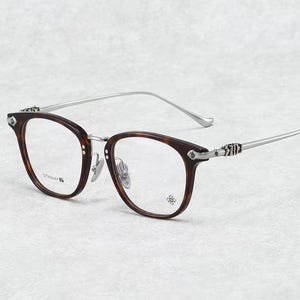 Op de afbeelding: Bril met een montuur in schildpadmotief en zilverkleurige pootjes. De glazen zijn helder en het montuur heeft een decoratief ontwerp op de slapen en hoeken. De tekst "TITANIUM" is zichtbaar op het montuur.