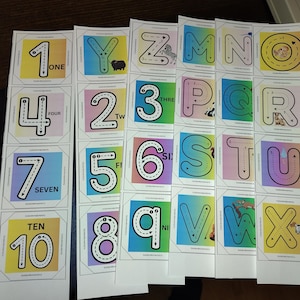 Op de afbeelding: Educatieve flashcards met cijfers en letters, elk met pijlen. De kaarten hebben kleurrijke achtergronden en bijpassende woorden. Ontworpen om kinderen te helpen cijfers en letters te leren schrijven.