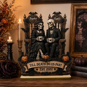 May include: A decorative figurine featuring two skeletons sitting on ornate thrones, each holding a small mug. The female skeleton is named Sophia and the male skeleton is named James. A banner at the base reads TILL DEATH DO US PART EST. 2012.