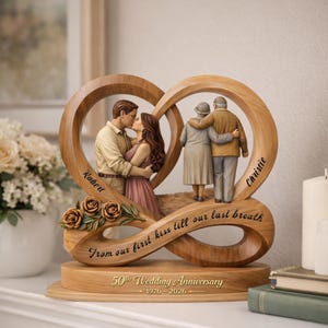 May include: A wooden infinity-shaped sculpture featuring a young couple kissing on the left and an elderly couple embracing on the right. It includes the text "Robert", "Christie", "From our first kiss till our last breath", and "50th Wedding Anniversary 1976-2026".