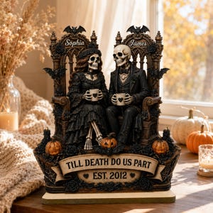 May include: A decorative figurine featuring two skeletons dressed in formal black attire, seated on ornate thrones. The names Sophia and James are inscribed above each figure. A banner at the base reads TILL DEATH DO US PART EST. 2012.