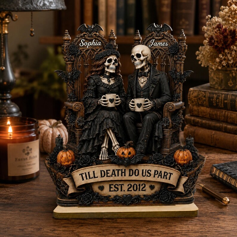May include: A decorative figurine featuring two skeletons seated on ornate thrones, holding mugs with heart icons. The base displays the text TILL DEATH DO US PART EST. 2012, accented with small pumpkins, bats, and roses. The names Sophia and James are inscribed above each skeleton.