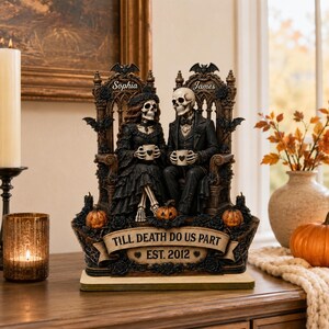 May include: A decorative figurine featuring two skeletons seated on ornate thrones, holding mugs. The base displays the text "TILL DEATH DO US PART" and "EST. 2012". The names "Sophia" and "James" are engraved on the thrones, surrounded by bats and pumpkins.