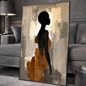 Puede incluir: Una impresión artística enmarcada que representa una silueta negra de una persona con un vestido. La obra de arte tiene un fondo beige y dorado. La impresión se exhibe en un salón, apoyada contra una pared.