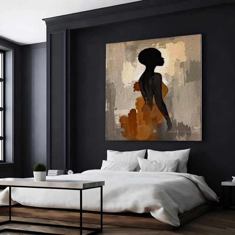 K&ouml;nnte beinhalten: Ein quadratisches Wandbild mit der schwarzen Silhouette einer Person vor einem abstrakten Hintergrund aus strukturierten beigen, hellbraunen und rostorangen Pinselstrichen, das &uuml;ber einem Bett mit wei&szlig;er Bettw&auml;sche in einem dunklen Raum h&auml;ngt.