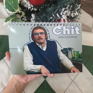 Puede incluir: Un calendario de espiral con la palabra "Chit" en letras azules y el año 2026. El calendario presenta a un hombre con gafas y bigote. La frase "Do it Lady M'yeah" está impresa en los bordes.