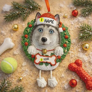 Può includere: Un ornamento natalizio a forma di cane husky con un cappello da Babbo Natale con la scritta "NAME". Il cane è circondato da una ghirlanda e tiene in mano un cartello a forma di osso con la scritta "2 YEAR". L'ornamento ha gli occhi blu ed è circondato da decorazioni.