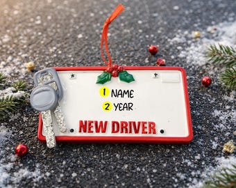 Può includere: Un ornamento a forma di targa bianca con bordo rosso, con la scritta "NEW DRIVER." e spazio per "NAME" e "YEAR." Chiavi d'auto argentate e nastro rosso. Decorazioni festive natalizie.