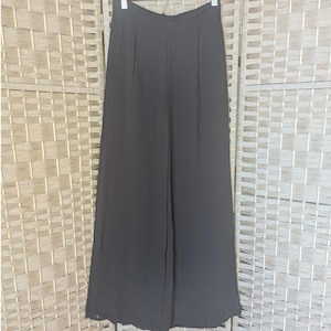 May include: A pair of black wide-leg pants hanging on a white hanger. The pants have a high waist and pleats at the front. The fabric appears to be lightweight and flowing, suitable for warmer weather.