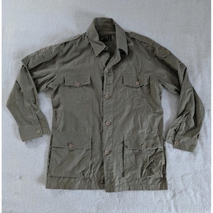 May include: Olive green jacket with four front pockets, button closures, and long sleeves. The jacket has a collared neckline and epaulettes on the shoulders. The fabric appears to be lightweight and slightly wrinkled.