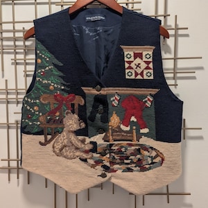 May include: A navy blue vest with a tapestry design featuring a Christmas tree, teddy bear, fireplace, and a decorative pattern. The vest has a button-up front and a beige bottom hem. The brand name "eagle eye" is visible on the label.