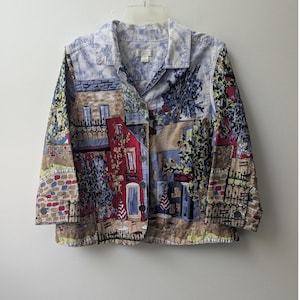 May include: A button-down jacket featuring a colorful, detailed print of a European-style street scene with buildings, trees, and outdoor cafe tables. The garment has a collared neckline, long sleeves with cuffs, and a multi-colored pattern.
