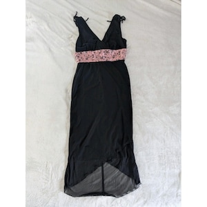 May include: A black sleeveless dress with a V-neckline and a pink floral patterned band at the waist. The dress has a flowing skirt with an asymmetrical hemline. The straps are tied at the shoulders.