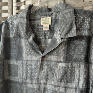 May include: Gray button-down shirt with a geometric pattern. The shirt has a collared neckline, a single chest pocket, and the brand label "L.L.Bean". The shirt is made of a lightweight fabric and has a relaxed fit.