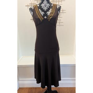 May include: A dark brown dress with a V-neckline and a flared skirt. The neckline is embellished with gold-colored beads. The dress is displayed on a black dress form against a white wall.