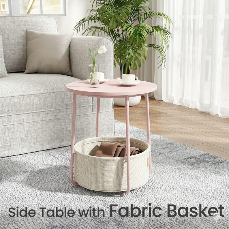 May include: A pink side table with a round top and a fabric basket. The table has a light pink metal frame and a beige fabric basket. The text "Side Table with Fabric Basket" is at the bottom of the image.