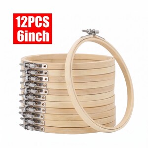 May include: A set of 12 pieces of 6-inch embroidery hoops made of light-coloured wood. Each circular hoop features a silver-toned metal tension screw mechanism at the top for securing fabric. The text 12PCS 6inch is visible in red.