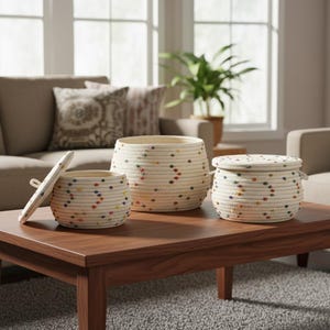 May include: Three cream-coloured rope baskets with colourful dot accents sit on a dark wood coffee table. The largest basket is open, the middle basket is open, and the smallest basket has a lid. The baskets are in a living room setting.