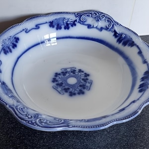 May include: A white and blue porcelain bowl with a scalloped edge. The bowl has a blue floral pattern around the rim and in the centre. The bowl is empty and sits on a dark surface.
