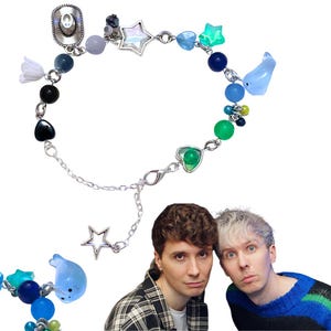 May include: A quirky bracelet with a silver chain and assorted charms. It features a cowboy hat, star, heart, and whale charms, alongside blue, green, and black beads. The bracelet is secured with a lobster clasp.
