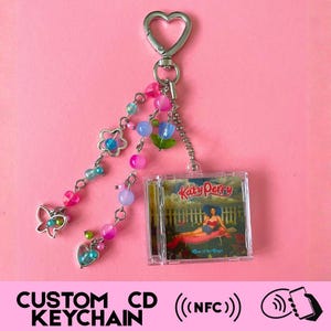 May include: A custom CD keychain with a miniature CD case displaying Katy Perry's album cover. The keychain includes a heart-shaped clasp and decorative beaded charms in shades of pink, blue, and green. The text at the bottom says "CUSTOM CD KEYCHAIN".