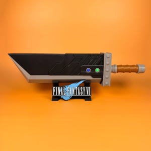 May include: A replica Buster Sword from Final Fantasy VII, in black and grey, with a brown handle and grey details. The sword is displayed on a black stand featuring the Final Fantasy VII logo in blue and white.