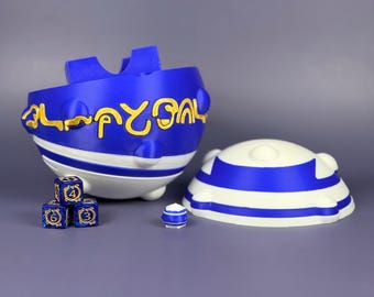 May include: A blue and white dice box with a matching lid and dice. The box has gold lettering and a unique shape. The dice are blue with gold numbers. A small, matching blue and white piece is also present.
