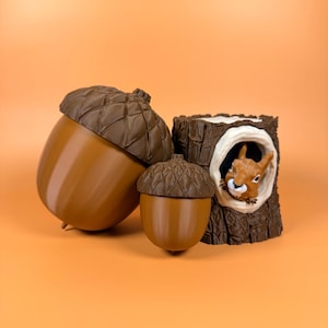 May include: Three brown decorative items: two acorn-shaped containers and a tree stump with a squirrel peeking out. The acorns have textured caps and smooth bodies. The squirrel is brown and white.