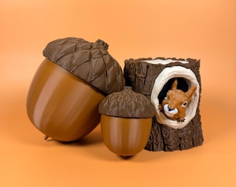 May include: Three brown decorative items: two acorn-shaped containers and a tree stump with a squirrel peeking out. The acorns have textured caps and smooth bodies. The squirrel is brown and white.