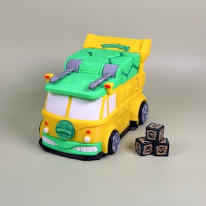 Könnte beinhalten: Ein gelb-grünes Spielzeugfahrzeug mit dem Wort "Turtles" oben. Das Spielzeug hat silberfarbene Kanonen und eine grüne Frontstoßstange. Drei Würfel mit goldfarbenen Zahlen liegen neben dem Fahrzeug.