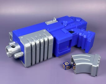 May include: A blue and grey toy gun with a detached magazine and two dice. The toy gun is mainly blue with grey accents and a detailed design. The magazine and dice are grey with blue and gold details.