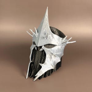 May include: A silver-colored helmet with a tall central spike and multiple smaller spikes around the crown. The helmet has a detailed, textured surface and a dark interior, suggesting a fantasy or cosplay theme.
