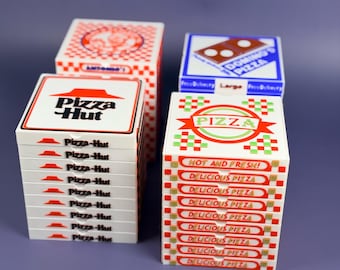 May include: A selection of small pizza boxes, featuring brands such as Pizza Hut and Domino's. The boxes are predominantly white, red, and blue, with printed text and logos, including "Delicious Pizza" and "Hot and Fresh!" on display.