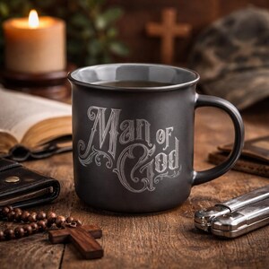 May include: A black ceramic mug with the words "Man of God" in an ornate font. The mug is filled with a dark liquid and sits on a wooden surface, alongside a rosary, a cross, and a lit candle.