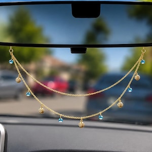 May include: A gold-toned metal car rearview mirror charm featuring two draped chains. The chains are adorned with small, evenly spaced metallic seashell charms and round, bright blue beads, creating a layered, dangling decorative accessory.