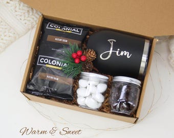 May include: A gift box with a black tumbler with "Jim" in silver script, two bags of "Colonial Hazelnut Cream" coffee, two small jars of candies, and festive greenery. The box is brown and the text "Warm & Sweet" is at the bottom.