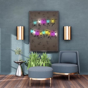 Könnte beinhalten: Ein gerahmtes Kunstwerk mit den Worten "MERRY CHRISTMAS" in einer stilisierten Schriftart, beleuchtet von bunten Lichterketten. Das Kunstwerk hängt über einem blauen Stuhl und Hocker mit goldenen Akzenten und schafft eine festliche Weihnachtsszene.