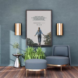 以下が含まれることがあります： テキストと人物の画像が印刷された額入りの部屋のシーン。青い椅子とオットマン、壁の燭台があります。小さな銀色のテーブルには植物があり、木製の床がシーンを完成させています。