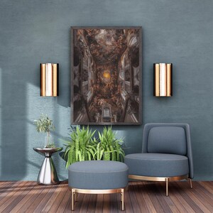 Puede incluir: Una moderna sala de estar con una obra de arte enmarcada que representa un detallado fresco del techo. La habitación incluye un sillón y un otomán azules con detalles dorados, dos apliques de pared y una pequeña mesa auxiliar con vegetación. El suelo es de madera.