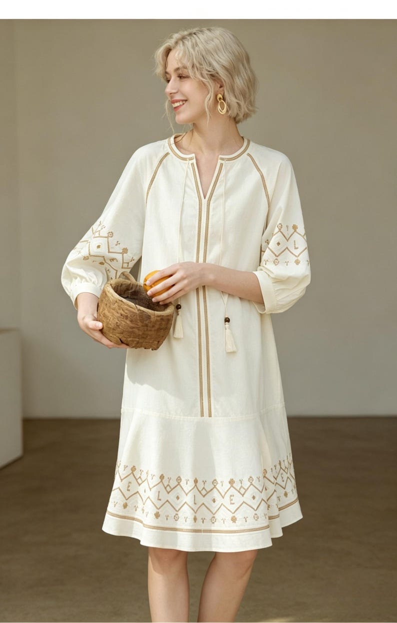 May include: Cream-colored dress with intricate brown embroidery. The dress features a V-neck, three-quarter sleeves, and a flared hem. The embroidery includes geometric and floral patterns. The dress is accessorized with tassels and is suitable for casual wear.