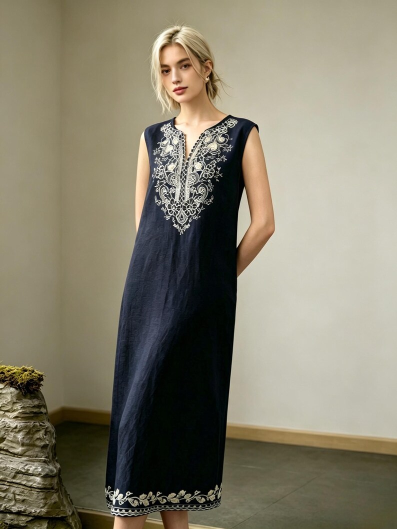 May include: A navy blue sleeveless dress with white floral embroidery. The dress has a V-neck and a relaxed fit. The embroidery is around the neckline and hem. The dress is a midi length, approximately 120 cm long, and is suitable for warm weather.