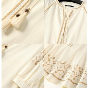 May include: Ivory-colored blouse with intricate embroidered details in a warm brown hue. Features a round neckline, long sleeves, and decorative tassels. The design includes geometric patterns and delicate stitching.