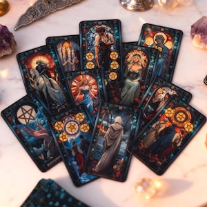 Könnte beinhalten: Ein Satz Tarotkarten mit farbenfrohen Illustrationen, die Figuren in Rahmen im Buntglasstil zeigen. Die Karten sind auf einer weißen Oberfläche angeordnet, umgeben von Kristallen und dekorativen Gegenständen. Die Kunstwerke zeigen verschiedene Symbole und Szenen.