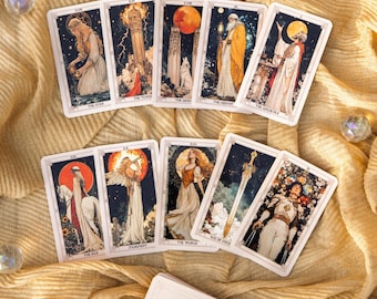 May include: A collection of tarot cards featuring detailed illustrations with celestial and mystical themes. The cards display images of figures, landscapes, and symbols in a vintage style, with titles like "The Star" and "The Tower". The cards are arranged on a golden fabric.