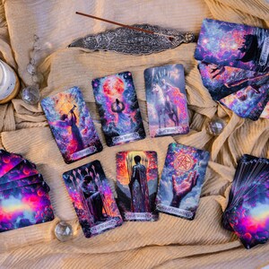 May include: A collection of tarot cards with vibrant, cosmic artwork. The cards feature illustrations of figures, celestial bodies, and symbols. The cards are arranged on a beige cloth, with a decorative incense holder and crystals.