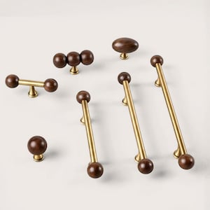 May include: A collection of wooden and brass cabinet hardware. The hardware includes knobs, pulls, and handles in various shapes and sizes. The wooden elements are a dark brown, and the metal is a warm brass color. The hardware is arranged on a white surface.