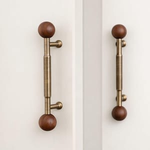 May include: Two door pulls with dark wood spheres. The pulls have a brass-coloured centre with a textured design. They are mounted on a white surface.